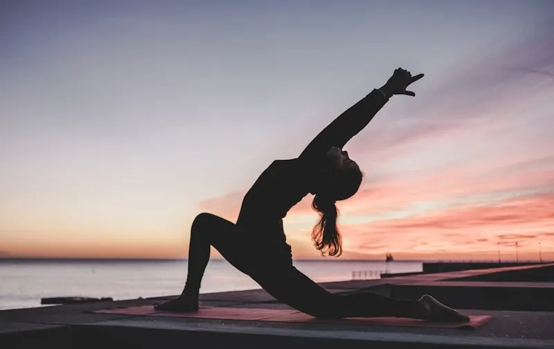 Silhouette of a person practising yoga by the water at sunset
