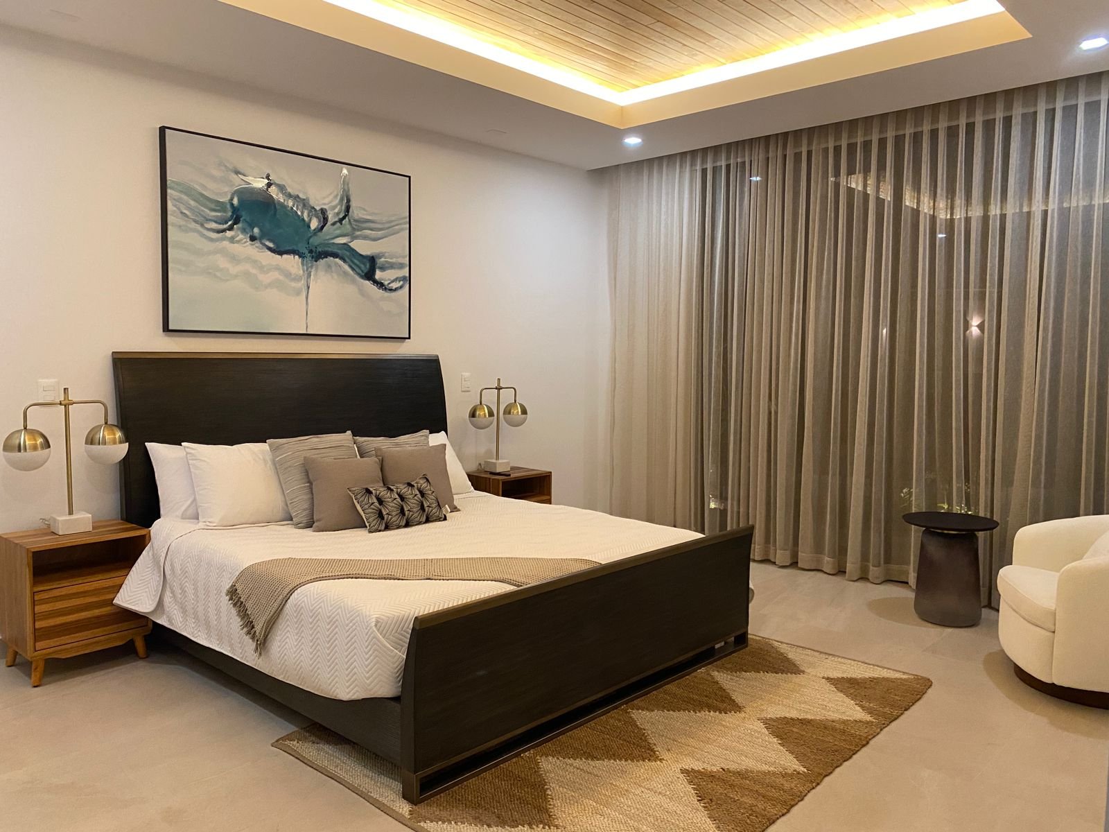 A bedroom with teak furnishings, abstract blue art, and warm cove lighting
